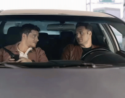 two men are sitting in a car and one is holding a cell phone