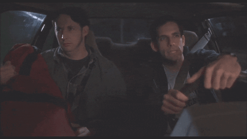 Two Men Are Sitting In A Car And One Of Them Is Holding A Red Bag GIF