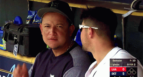 Two Men Are Sitting In A Dugout With A Scoreboard Behind Them That Says Bedrosian On It GIF