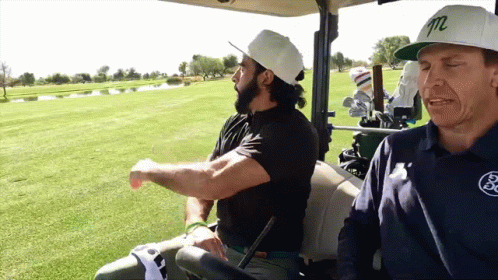 Two Men Are Sitting In A Golf Cart With One Wearing A White Hat With The Letter M On It GIF