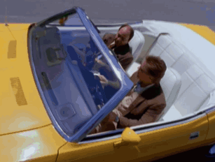 Two Men Are Sitting In A Yellow Convertible With The Roof Up GIF