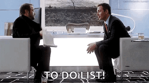 Two Men Are Sitting In Chairs In Front Of A Desk Talking To Each Other And One Of Them Is Holding A Laptop . GIF