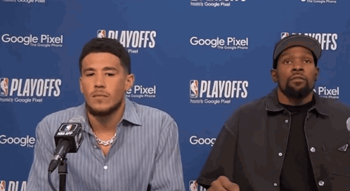 Two Men Are Sitting In Front Of A Google Pixel Sign GIF