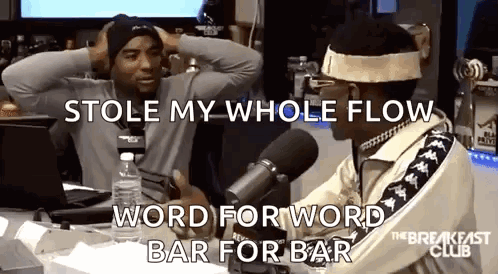 Two Men Are Sitting In Front Of A Microphone And One Of Them Is Holding His Head . GIF