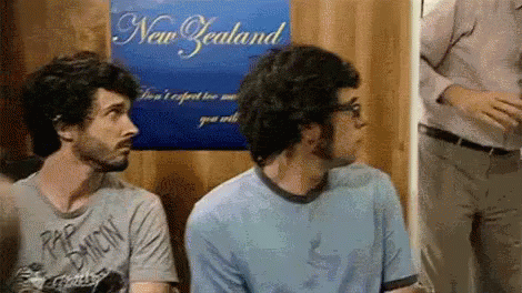 Two Men Are Sitting In Front Of A Poster That Says New Zealand GIF