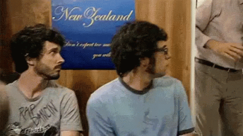 Two Men Are Sitting In Front Of A Poster That Says New Zealand GIF