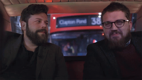 two men are sitting in front of a red bus that says clinton pond 36