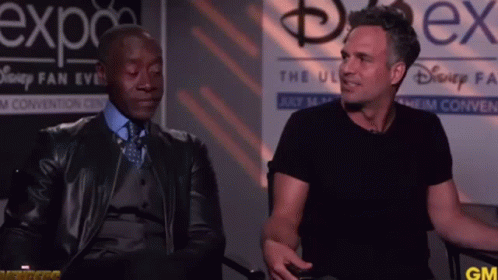 Two Men Are Sitting In Front Of A Sign That Says Disney Fan Expo GIF