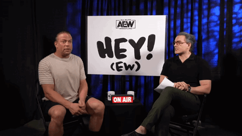 Two Men Are Sitting In Front Of A Sign That Says Hey ( Ew ) GIF