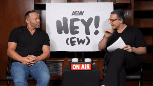 Two Men Are Sitting In Front Of A Sign That Says Hey ( Ew ) GIF