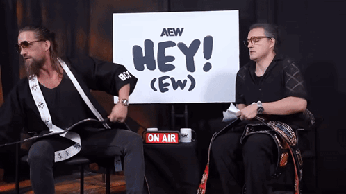 two men are sitting in front of a sign that says hey ( ew )