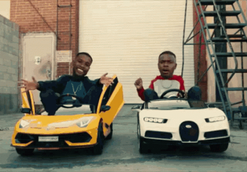 Two Men Are Sitting In Toy Cars With Their Doors Open And One Of Them Has A License Plate That Says ' Sd ' On It GIF