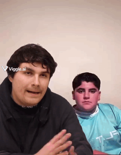 Two Men Are Sitting Next To Each Other And One Has A Viggle.ai Sticker On His Head GIF