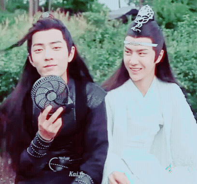 Two Men Are Sitting Next To Each Other And One Of Them Is Holding A Fan In His Hand . GIF