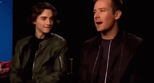Two Men Are Sitting Next To Each Other In A Dark Room And Talking To Each Other . GIF
