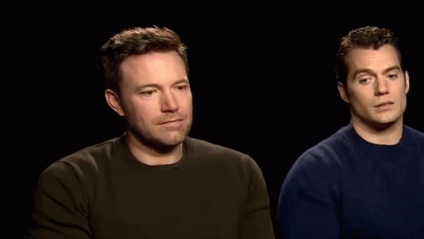 Two Men Are Sitting Next To Each Other In A Dark Room And Talking To Each Other . GIF
