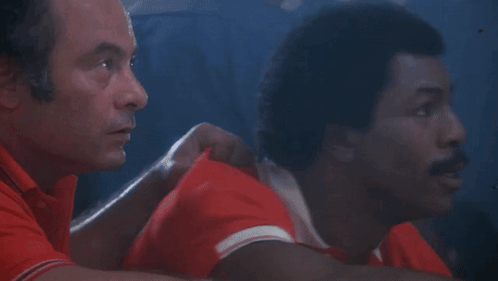 Two Men Are Sitting Next To Each Other In A Dark Room . GIF