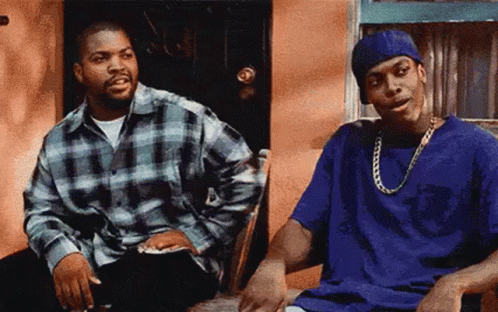 Two Men Are Sitting Next To Each Other In Front Of A Building . GIF