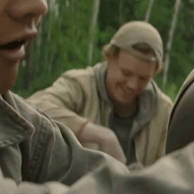 Two Men Are Sitting Next To Each Other In The Woods . GIF