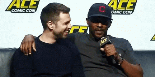 Two Men Are Sitting Next To Each Other On A Couch . One Of The Men Is Wearing A Hat . GIF