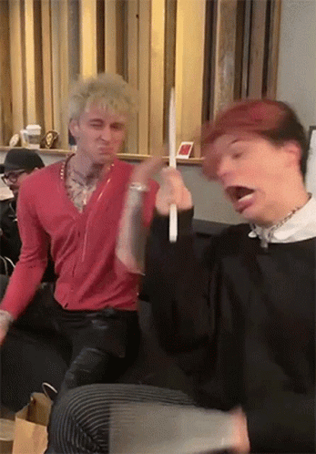 Two Men Are Sitting Next To Each Other On A Couch Playing With A Toy . GIF