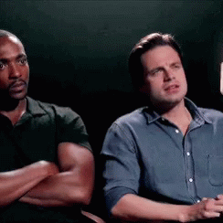 Two Men Are Sitting Next To Each Other With Their Arms Crossed And Looking At Something . GIF