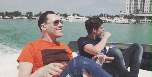 Two Men Are Sitting On A Boat In The Water And One Has A Bottle Of Aquafina Water In His Hand GIF