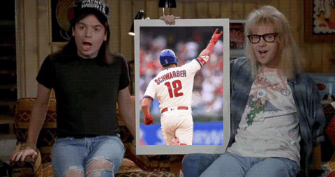 Two Men Are Sitting On A Couch And One Is Holding A Framed Picture Of Schwarber 12 GIF