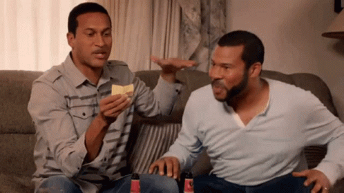 Two Men Are Sitting On A Couch And One Of Them Is Holding A Chip In His Hand GIF