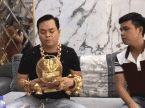 Two Men Are Sitting On A Couch And One Of Them Is Wearing A Gold Necklace And Bracelets GIF