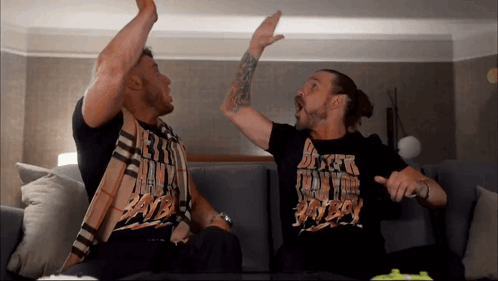Two Men Are Sitting On A Couch And One Of Them Is Wearing A Shirt That Says ' Dirty Boy ' GIF