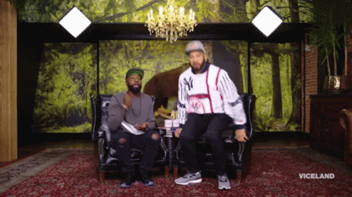 Two Men Are Sitting On A Couch In Front Of A Wall With Trees And The Word Viceland On It GIF