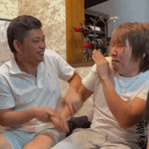 Two Men Are Sitting On A Couch Talking To Each Other And One Has A Bottle Of Wine In The Background GIF
