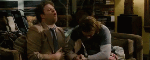 Two Men Are Sitting On A Couch Talking To Each Other . GIF