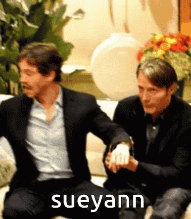 Two Men Are Sitting On A Couch With The Name Sueyann On The Bottom Right GIF