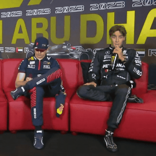 Two Men Sitting On Red Couch In Front Of Tabu Dha Sign GIF
