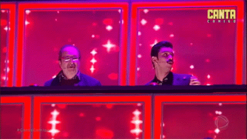 Two Men Are Sitting On A Stage In Front Of A Pink Background . GIF