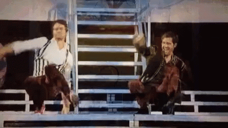 Two Men Are Sitting On A Stage With Their Arms Outstretched And A Dog In The Background . GIF