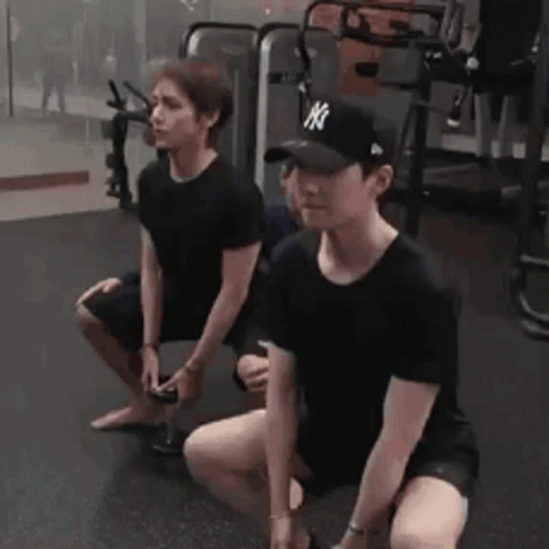 Two Men Are Squatting Down In A Gym . One Of The Men Is Wearing A Ny Hat . GIF