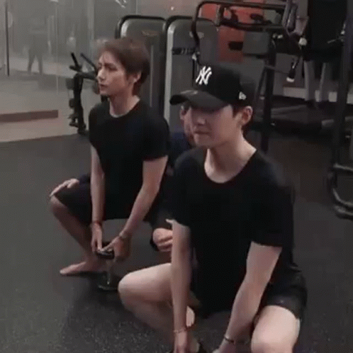 Two Men Are Squatting Down In A Gym While Holding Dumbbells . GIF