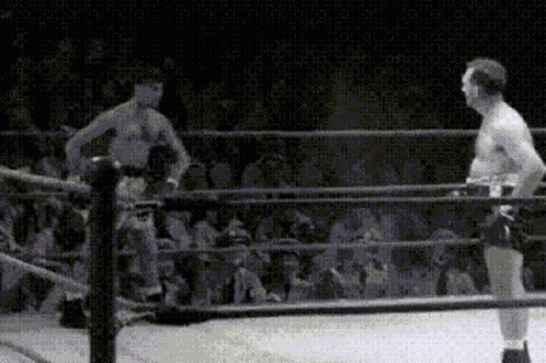 Two Men Are Standing In A Boxing Ring With A Crowd Watching Them . GIF