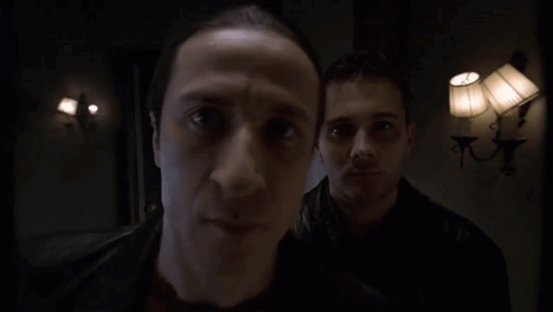 Two Men Are Standing In A Dark Room With Lamps On The Wall GIF