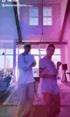 Two Men Are Standing In A Living Room With Purple Lights Behind Them And The Words Tik Tok On The Bottom GIF