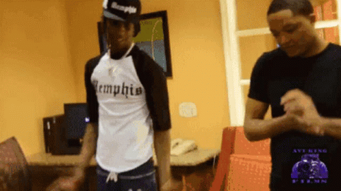 Two Men Are Standing In A Room And One Has A Shirt That Says Memphis On It GIF
