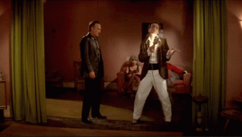 two men are standing in a room with a woman sitting in a chair