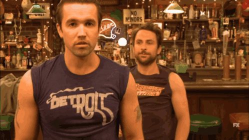 Two Men Are Standing In Front Of A Bar With One Wearing A Shirt That Says Detroit GIF