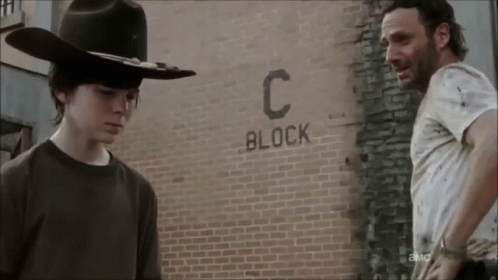 Two Men Are Standing In Front Of A Brick Wall That Says Block C. GIF