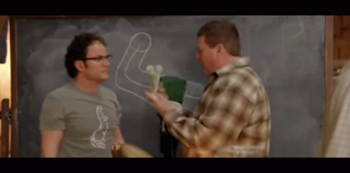 two men are standing in front of a chalkboard with a drawing of a penis on it
