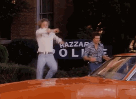 Two Men Are Standing In Front Of A Hazzard Police Sign GIF