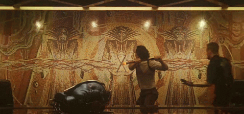 Two Men Are Standing In Front Of A Large Wall With A Drawing Of A Man With A Sword GIF